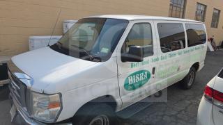 White Ford E350 van with business advertising on the side for "BISRA Glatt Kosher Meats," parked near a brick building.