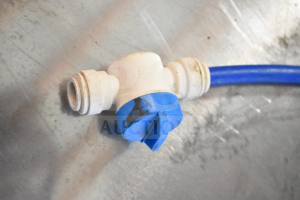 A white plastic T-connector with blue tubing attached on a metal surface, featuring a twist valve.