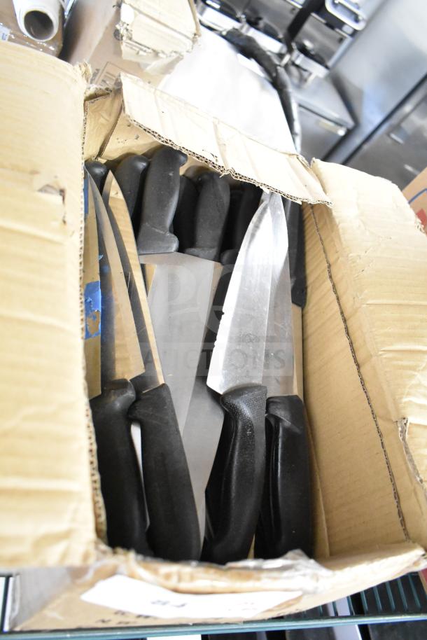 Open box of 50 sharpened stainless steel chef knives with black handles. Knives in new condition, ideal for professional use.