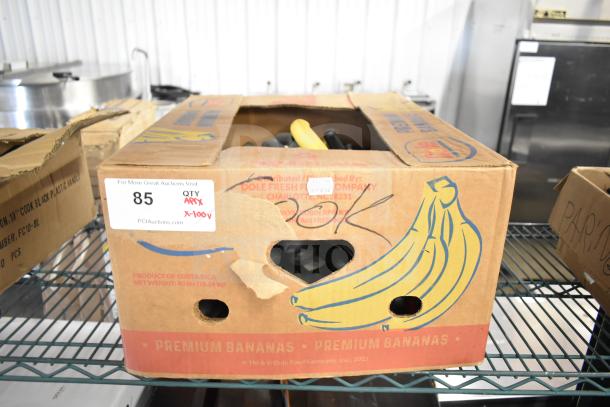 Brown box labeled "Premium Bananas" containing 100 sharpened stainless steel chef knives. Tag indicates auction info and quantity.