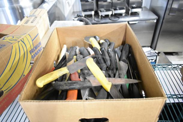 Box of 100 assorted sharpened stainless steel chef knives with colored handles, stored in good condition.