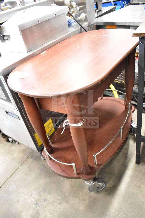 Geneva wooden table with under shelf, commercial casters. Brown finish, minor surface wear, metal rails on lower shelf.