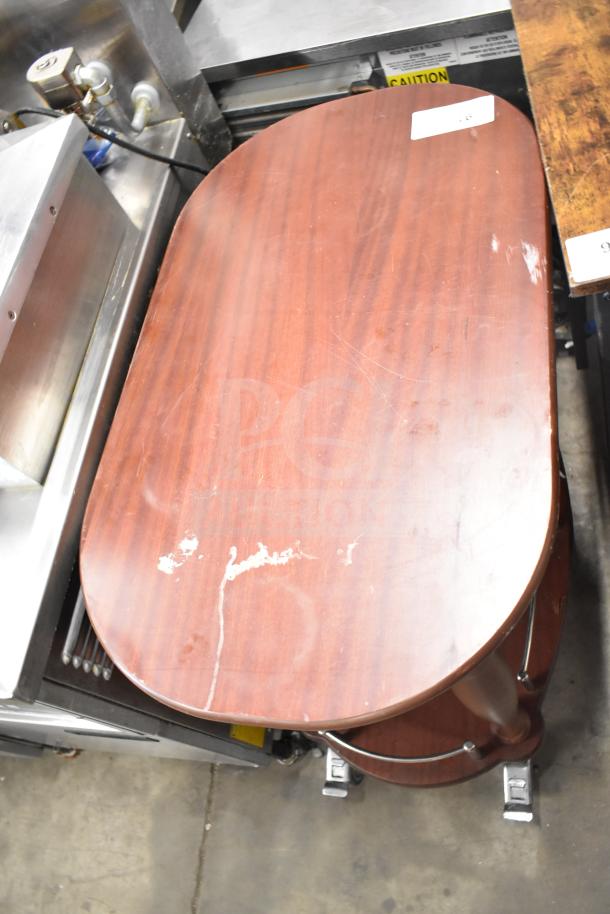 Geneva wooden table with under shelf, oval shape, commercial casters, surface wear visible, auction tag attached.