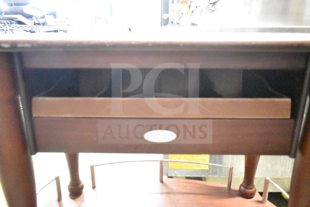 Geneva Wooden Table with under shelf, commercial casters; visible front drawer, rounded legs, and dark finish.