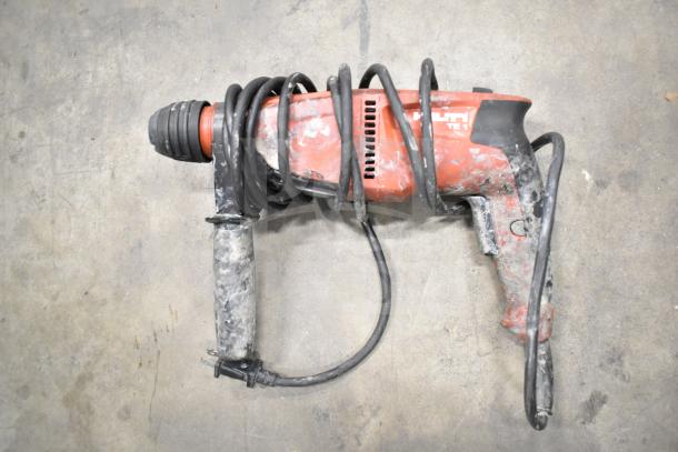 Hilti TE1 rotary hammer drill, red and black, in used condition with visible wear, coiled power cord, placed on concrete floor.