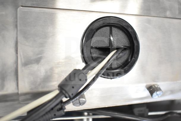 Close-up of a metal device with cables emerging from a circular outlet, part of a kitchen armor monitor or thin client mini PC.