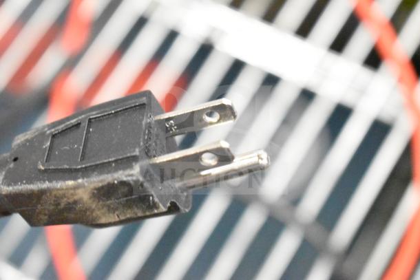 Close-up of a black power plug with two metal prongs, showing wear on the surface, against a blurred striped background.