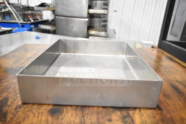 Stainless steel metal bin on wooden table, showing minor wear, with a barcode label inside.