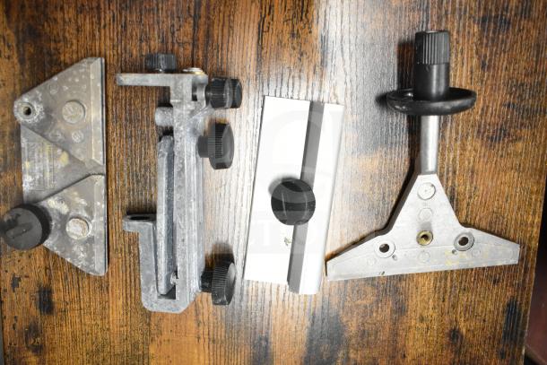 Lot of various metal tool parts on wooden surface, featuring knobs and adjustment mechanisms, in used condition.