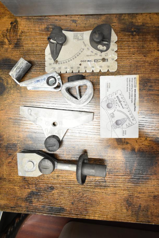 Lot of various metal parts, including a gauge and knobs, displayed on a wooden surface. Condition appears used.