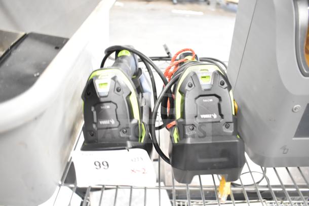 Two Zebra DS3578 barcode scanners in good condition with visible labels, cords, and charging docks on a metal shelf.