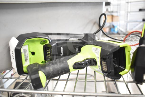 Two Zebra DS3578 barcode scanners, rugged design, green accents, visible labels, on metal shelf. Scuff marks present.