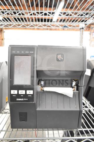 Zebra ZT411 Industrial Barcode Printer, black, with touchscreen, paper feed visible, used condition, on metal shelf.