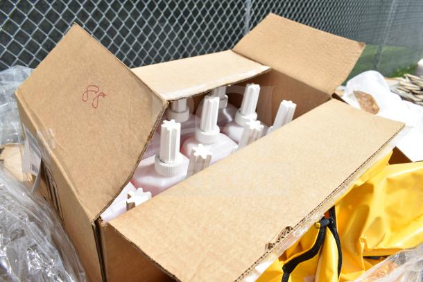 Open cardboard box containing new bottles with white caps, possibly powdered hand soap, on a sunny day.