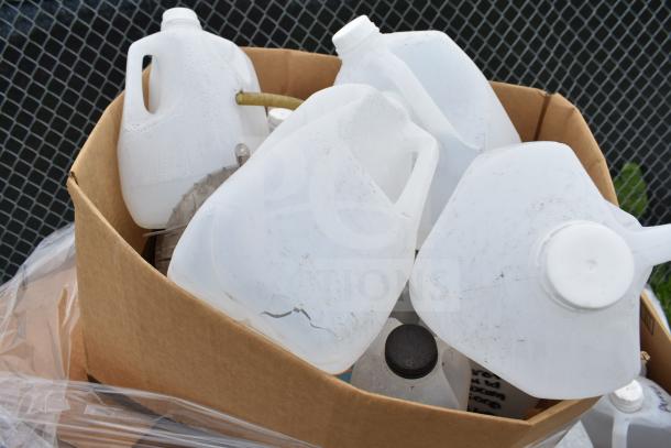 Cardboard box containing various scratched and dented plastic cleaners and vinegar bottles, mostly gallon size.