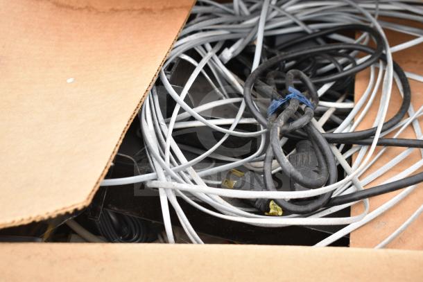 Box of assorted cables and cords, new with possible scratches or dents. Various lengths and types visible, no labels present.