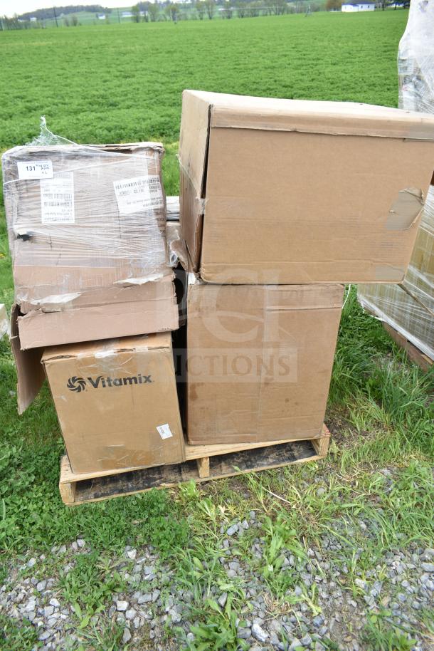 Cardboard boxes on a pallet, including a Vitamix-branded box, indicating new scratch and dent items for auction.