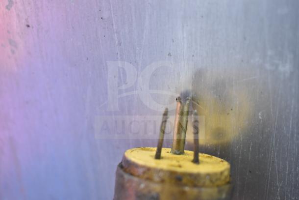 Corroded three-prong electrical plug against a metallic surface, close-up view showing damage and rust.