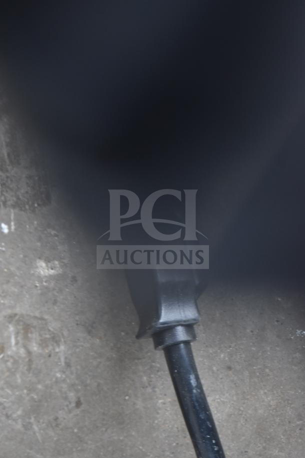 Blurry image showing a black cord against a concrete surface, details unclear.