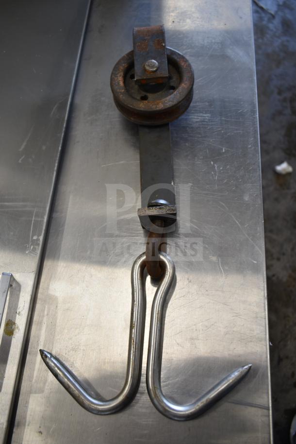 Iron trolley roller with attached dual hooks; rusted condition, industrial design, ideal for machinery or decor.