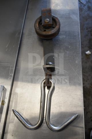 Iron trolley roller with attached dual hooks; rusted condition, industrial design, ideal for machinery or decor.