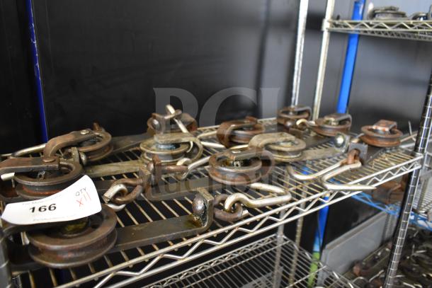 11 trolley rollers on metal shelves, used condition. Features hooks and pulleys. Tag marked "166, QTY XII".