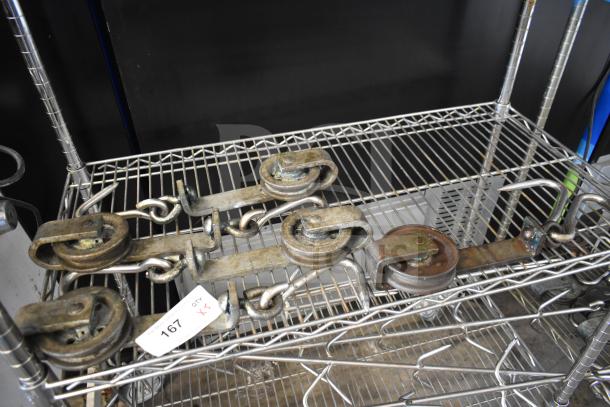 Five vintage metal trolley rollers on a wire shelf. Condition shows signs of rust and wear. Tag indicates quantity five.