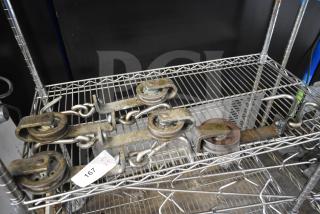 Five vintage metal trolley rollers on a wire shelf. Condition shows signs of rust and wear. Tag indicates quantity five.