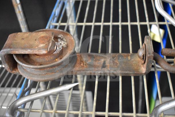 Rusty trolley roller with hook meat hanger on metal shelf, showing signs of wear. Auction includes three items.