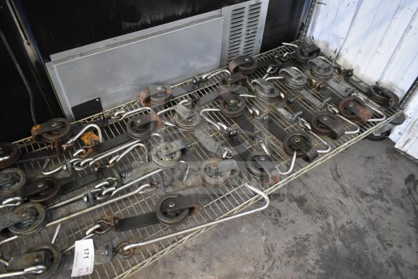 24 trolley rollers and hook meat hangers on a wire rack in used condition. Includes tag number 171.