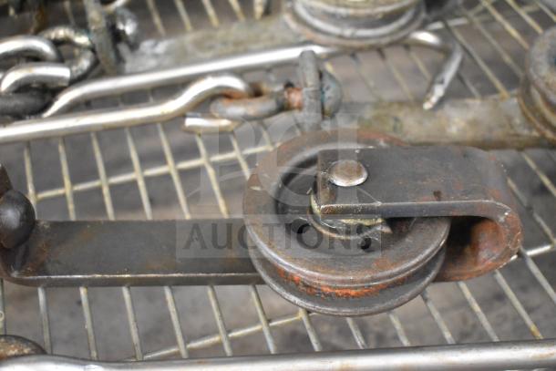 24 heavy-duty metal trolley rollers for meat hanging, showing wear but functional. Chains and hooks attached.