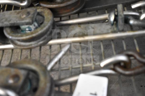 24 metal trolley rollers with hooks, used for meat hanging. Visible wear, sturdy build. Includes multiple sets for bulk auction.