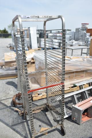 Commercial pan transport rack on casters with metal frame, multiple shelves, marked "KSTONE CATERING," showing some wear.