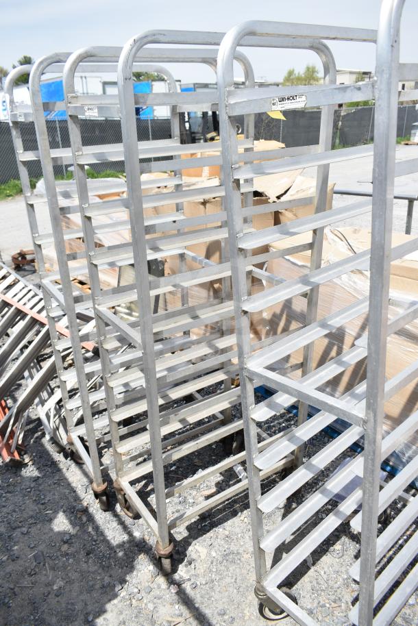 Three commercial pan transport racks on casters, aluminum, Win-Holt brand, used condition, with visible manufacturer's label.