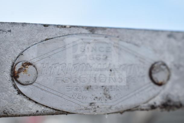 Close-up of a metal plaque on a commercial double pan transport rack. Reads "Friedmans, Since 1889, Food Service Equipment, New York City."
