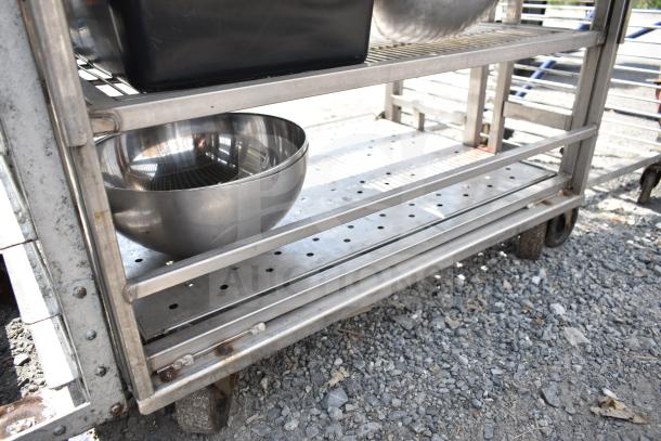 Commercial transport rack with casters, housing various metal bowls. Sturdy metal shelves, slight rust on edges.
