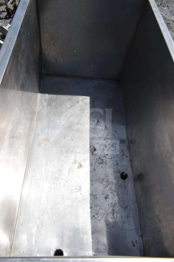Commercial portable bin with metal interior, visible wear, and drainage holes. Mounted on heavy-duty casters for mobility.