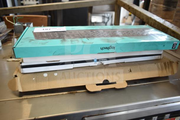 Stack of four brand new keyboards in boxes, including Logitech and Onn models. Boxes show minor scratches and dents.