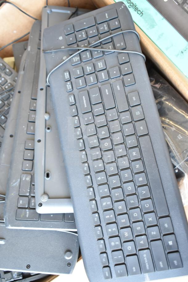Various keyboards stacked on a pallet, mostly black, some showing Logitech branding, mixed condition.
