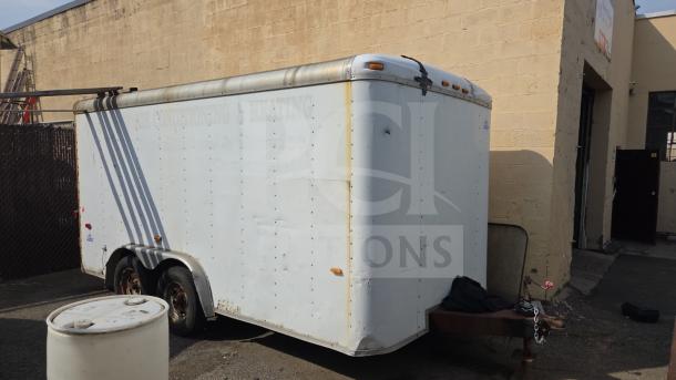 US Cargo 16' enclosed trailer, white exterior, dual axles, visible wear. Features side lighting and rear door access.