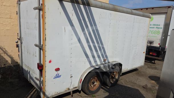 US Cargo 16' enclosed trailer, white exterior, visible rust, dual axle. Features secure locking system, shows wear.