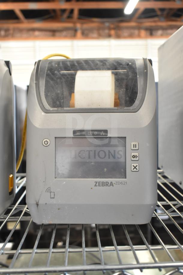 Zebra ZD621 desktop direct thermal barcode printer, gray, touchscreen, slight wear, visible branding, on metal shelf.