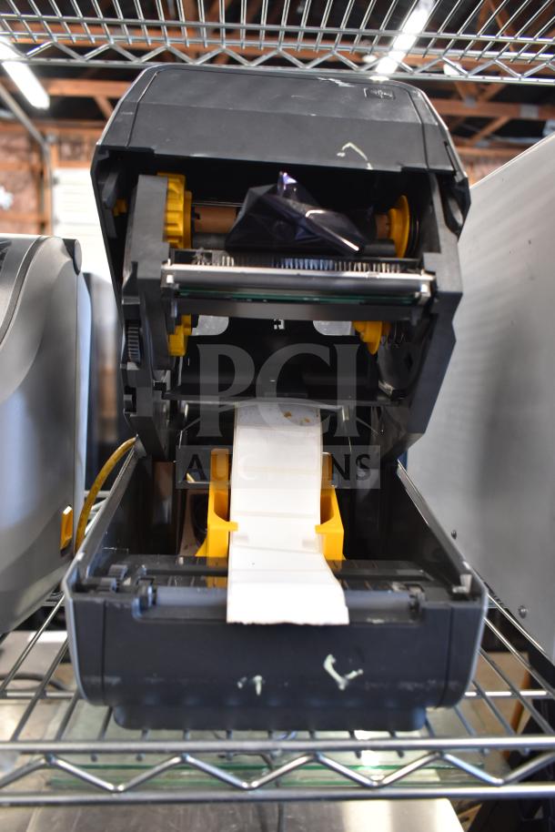 Two Zebra ZD621 desktop direct thermal barcode printers on a metal shelf, open with visible label roll, in used condition.