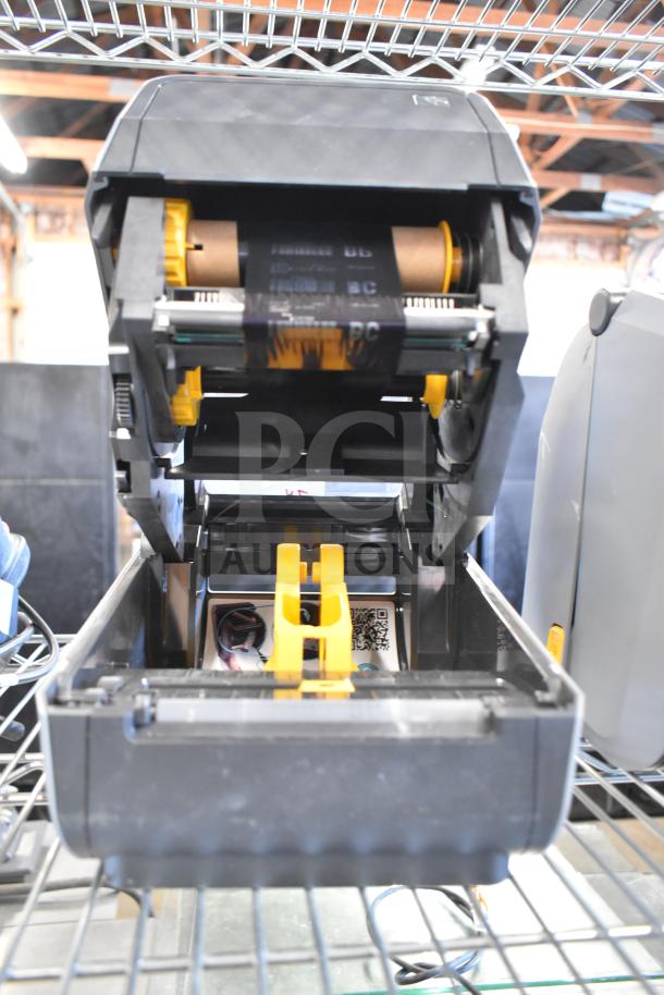 Zebra ZD621 desktop direct thermal barcode printer open view, showing internal components, in good condition on a metal shelf.