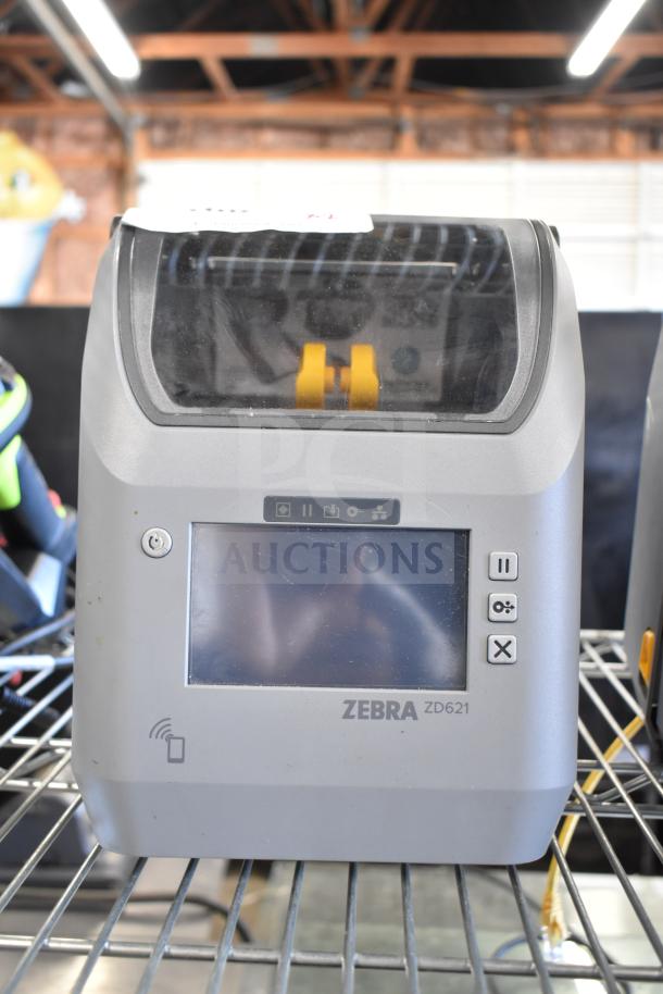 Two Zebra ZD621 desktop direct thermal barcode printers, shown on a metal shelf. Features include touchscreen and connectivity icons.