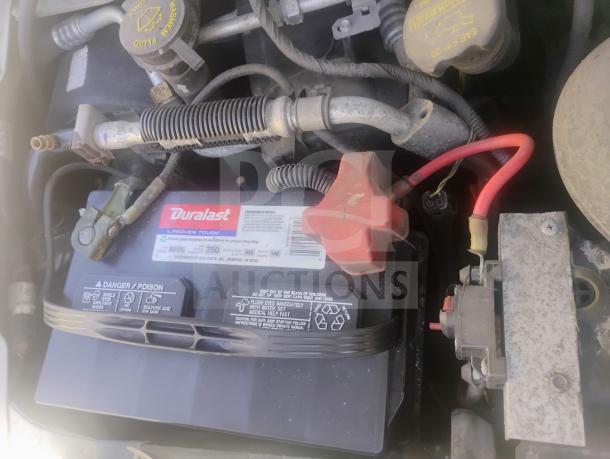 Engine view of a 2010 Ford E350 Cargo Van. Visible Duralast battery with label details, wiring, and fluid caps.