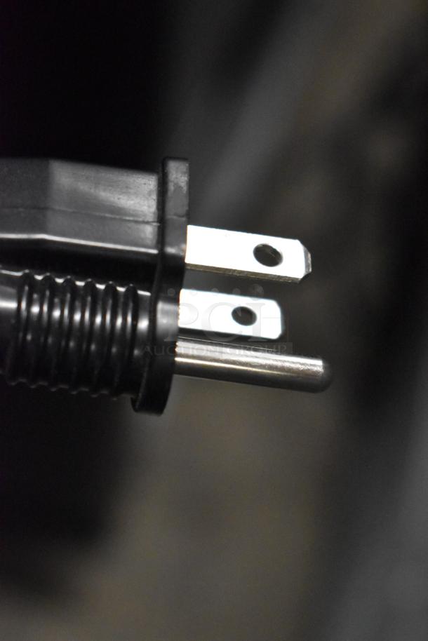 Close-up of a black electrical plug with two metal prongs against a dark background.