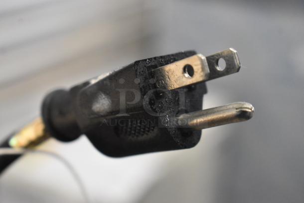 A close-up of a black electrical plug with metal prongs, showing slight wear and dust.