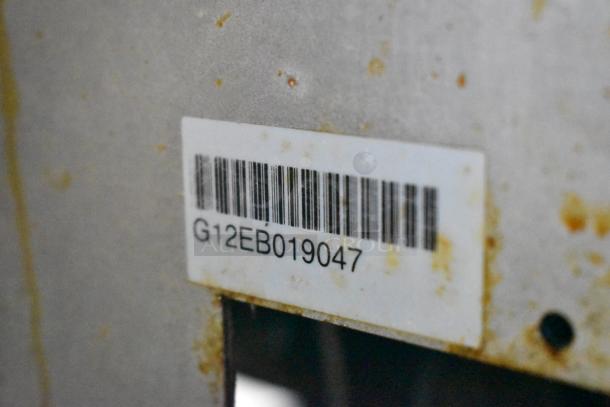 Barcode and label "G12EB019047" on stainless steel surface of Pitco Frialator deep fat fryer. Visible wear and stains.