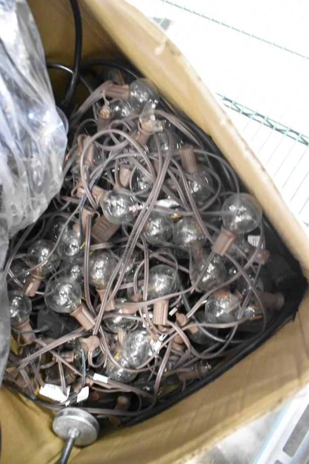 Box of various items featuring tangled string lights, brown cords, and clear bulbs. Condition appears used.